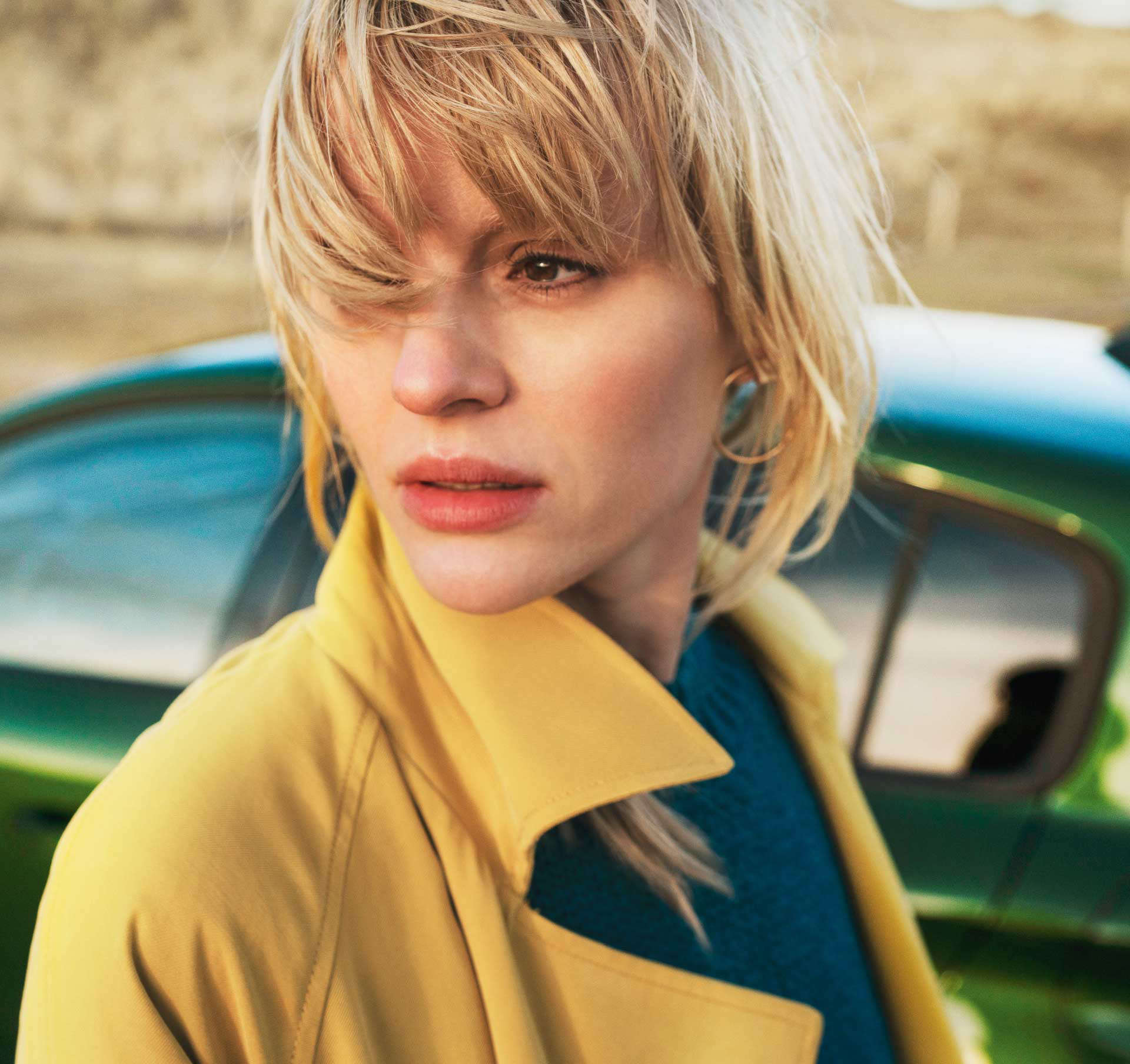 Жінка у жовтому плащі стоїть біля автомобіля Peugeot